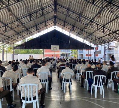 Imagem de alunos sentados em cadeiras de plástico na cor branca, em uma quadra de futebol. Ao fundo, o Time Acolher, grupo que realizou a ação.